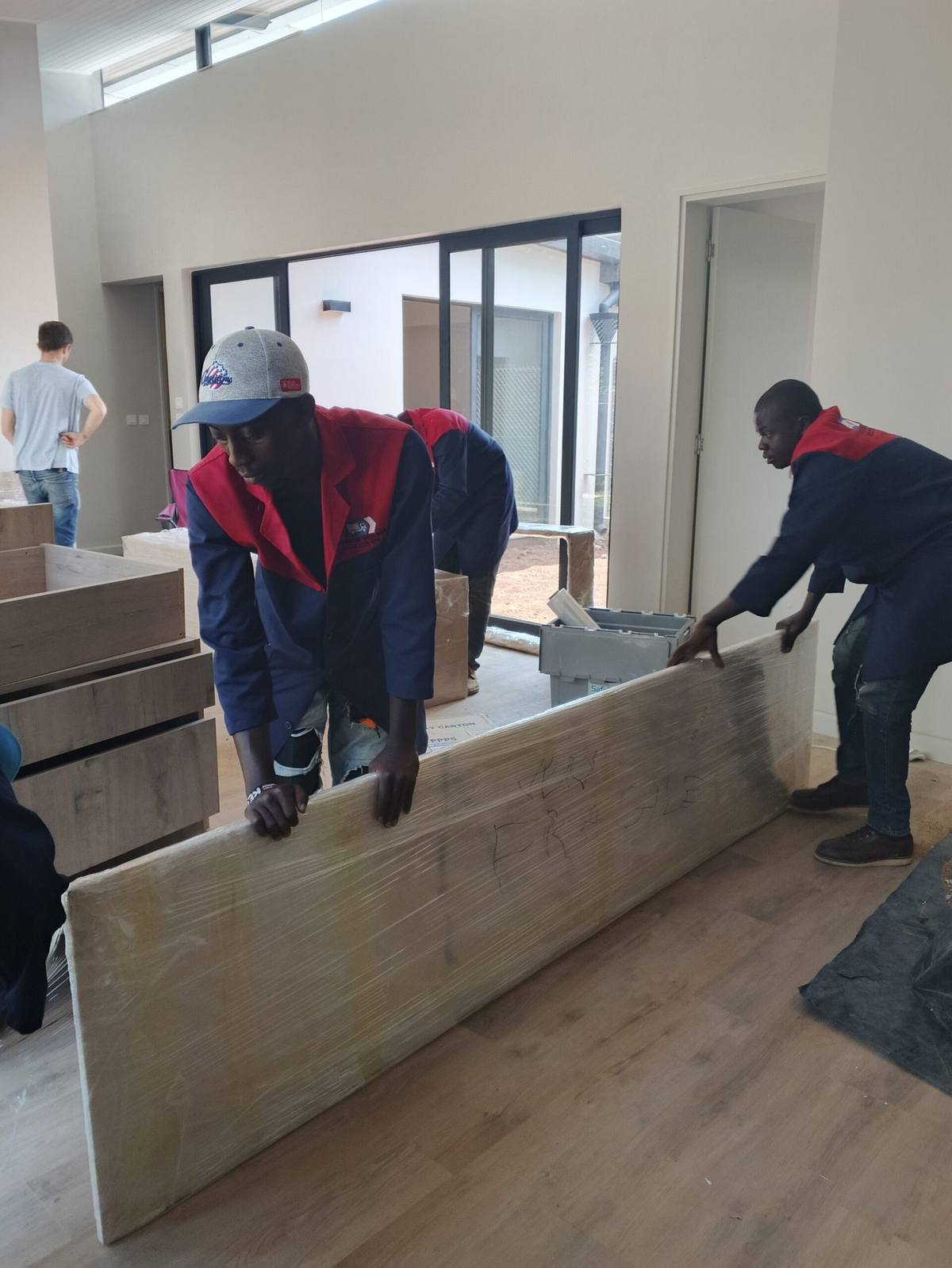 Two movers carrying a wrapped sofa out of a Nairobi home